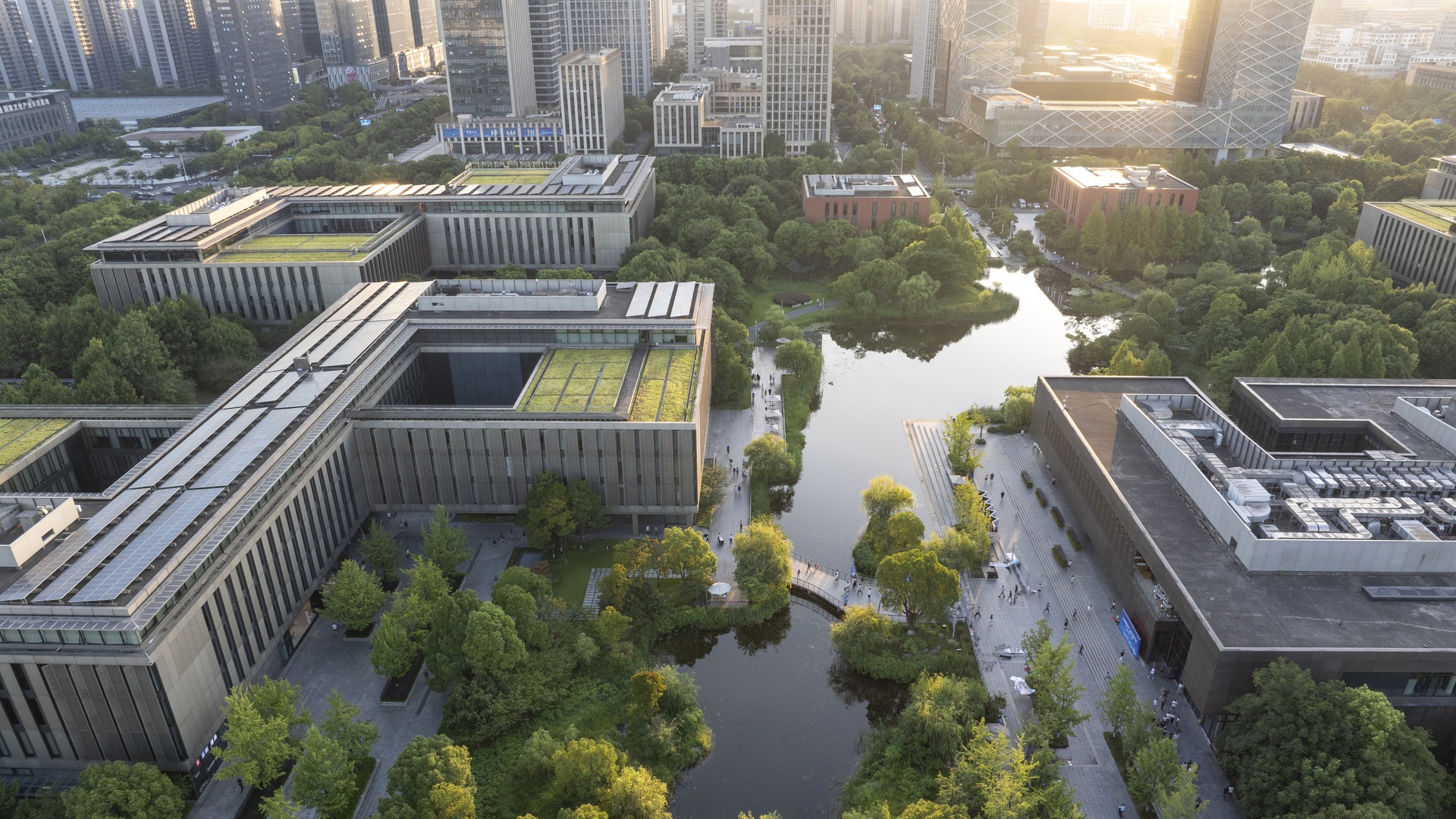 Luftaufnahme von Hightech-Forschungs- und Bildungsgebäuden, die in eine nachhaltige Landschaftsgestaltung und Wasserspiele integriert sind, bei Sonnenuntergang.