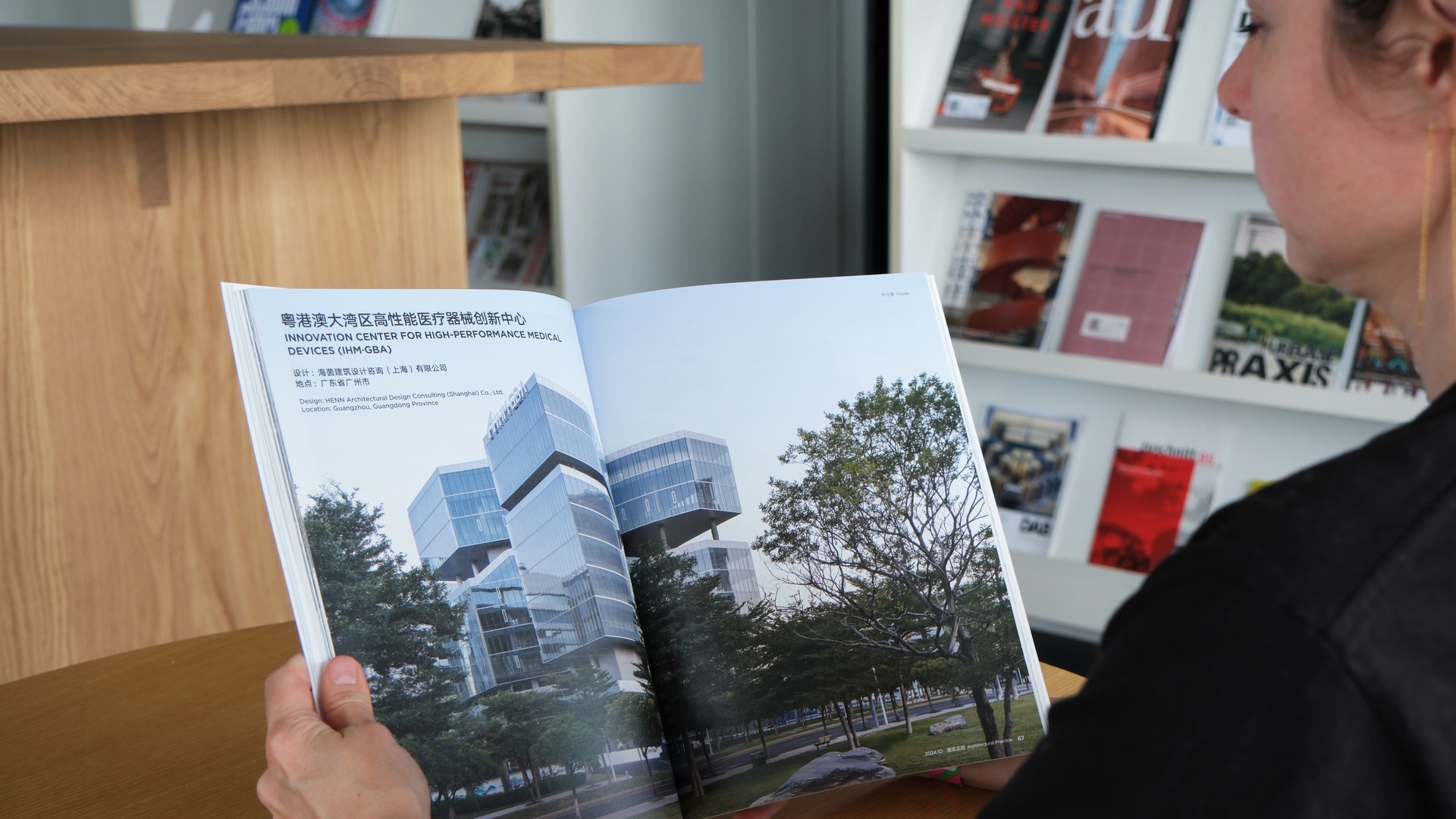 Person, die eine Zeitschrift liest, in der eine hochmoderne Forschungseinrichtung aus Glas vorgestellt wird, die innovative, nachhaltige Architektur inmitten von Grünanlagen präsentiert.