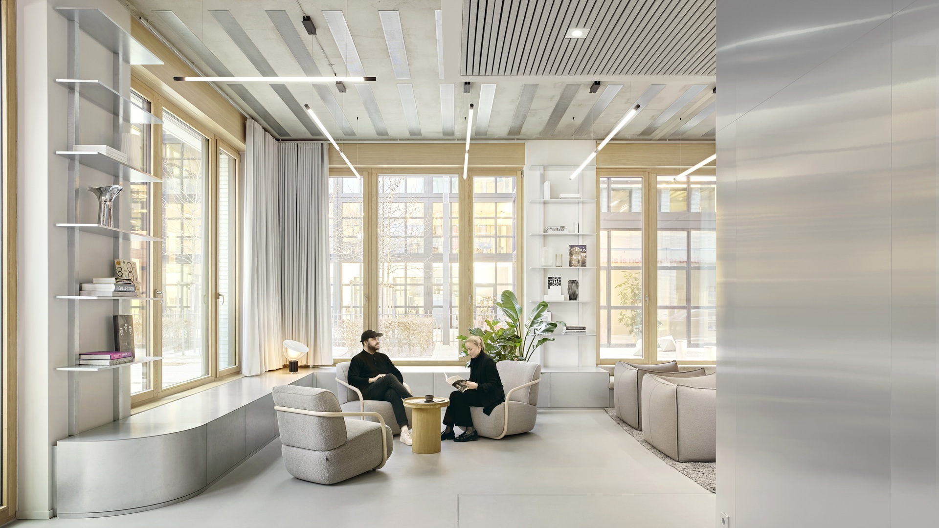 Zwei Personen arbeiten in einer lichtdurchfluteten, minimalistischen Lounge mit großen Fenstern, nachhaltigen Materialien und fortschrittlichen technischen Integrationen zusammen.