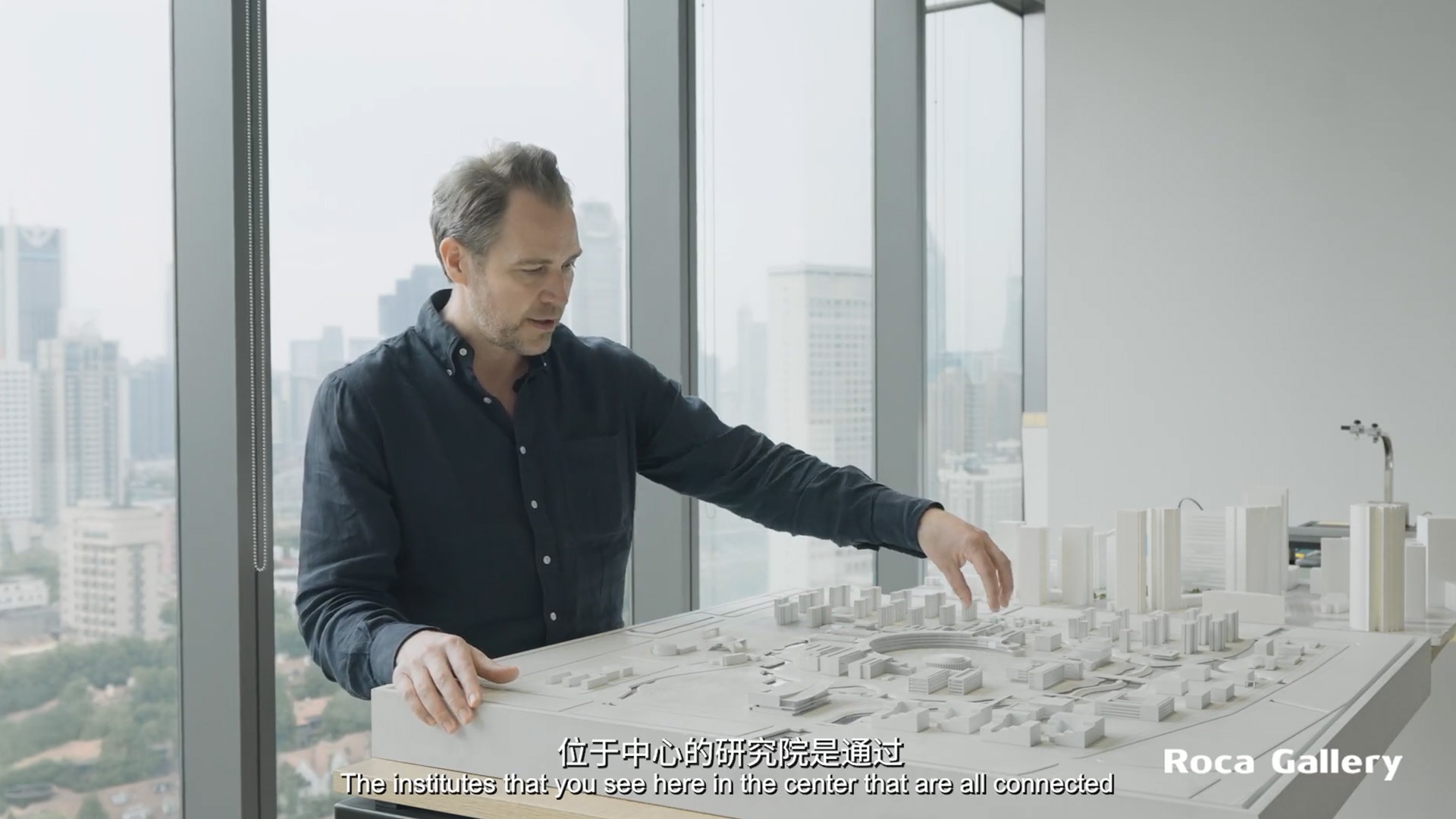 Ein Architekt stellt ein Modell fortschrittlicher, nachhaltiger Forschungs- und Industriegebäude am Fenster vor und hebt das innovative Design hervor.