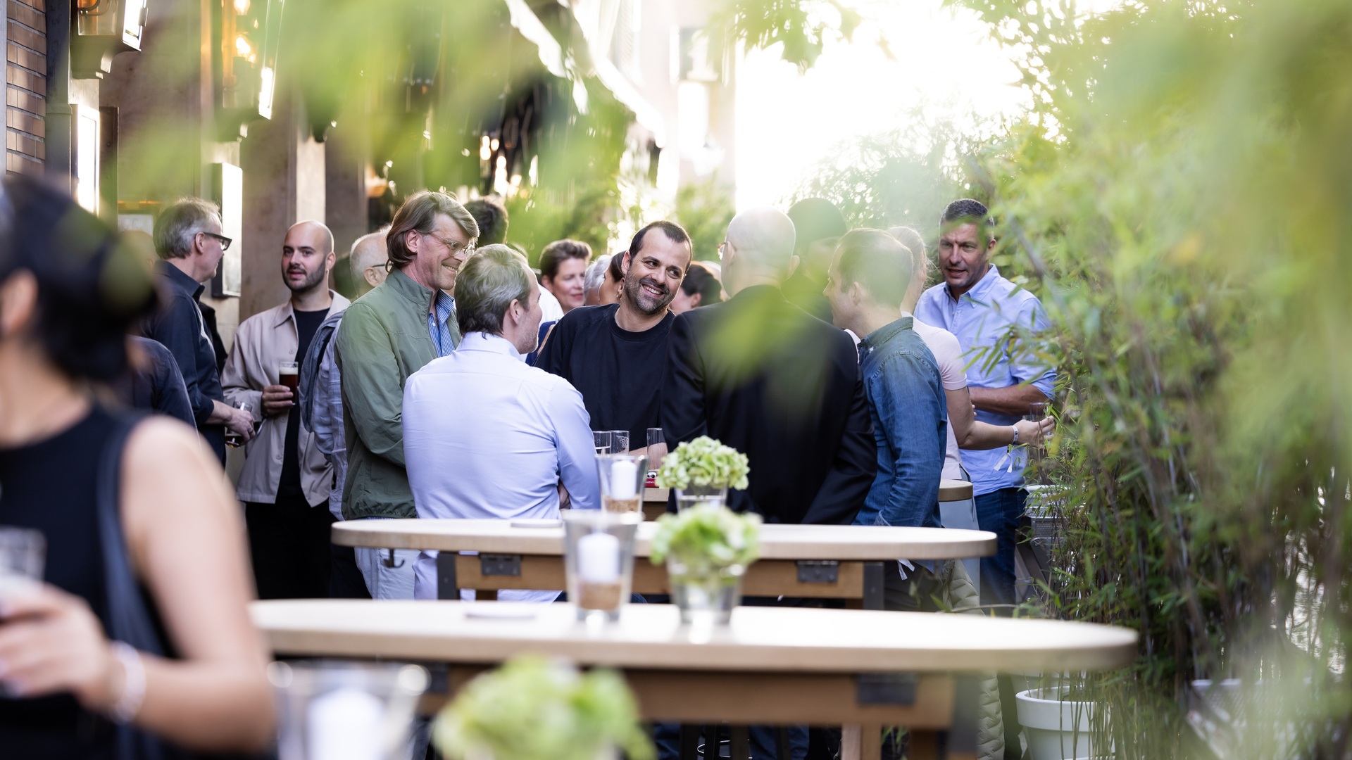 Bei einer Veranstaltung im Freien treffen sich die Gäste an modernen, hohen Tischen, umrahmt von nachhaltiger Landschaftsgestaltung und energieeffizienter Raumbeleuchtung.