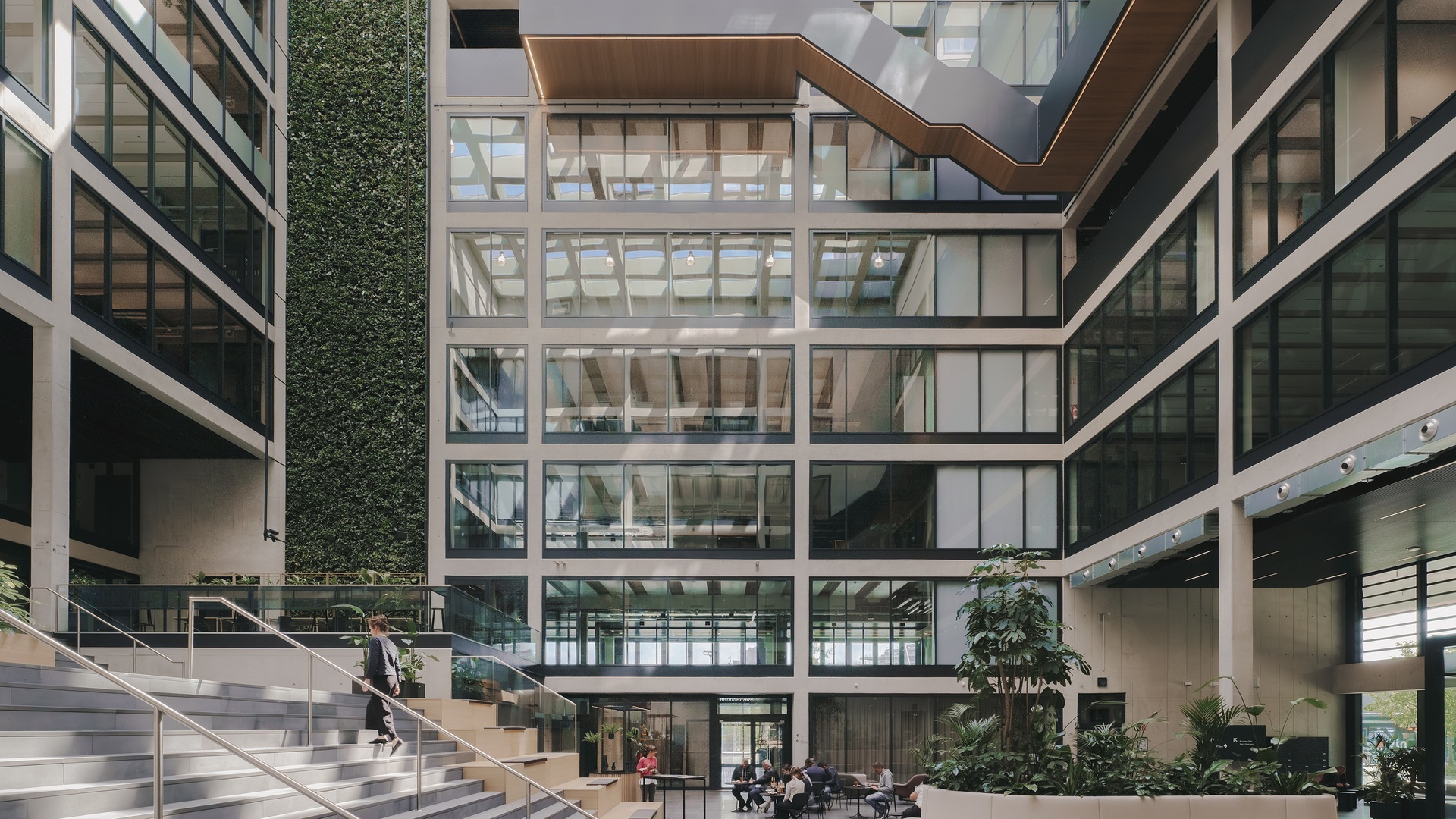 Innovatives Atrium mit Glaswänden, Begrünung, integrierter Technik und gemeinschaftlichen Sitzgelegenheiten - konzipiert für Forschung und industrielle Spitzenleistungen.