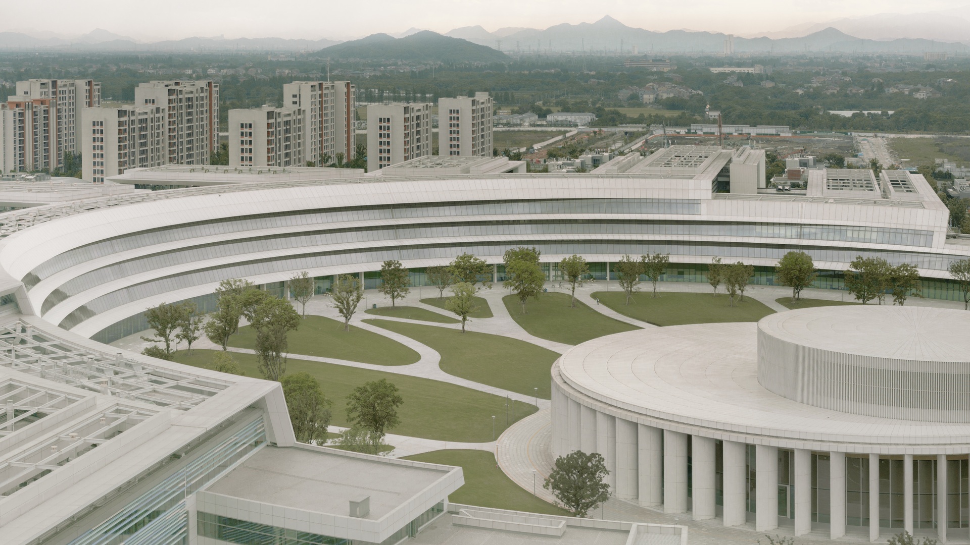 Innovativer, geschwungener Bürokomplex mit begrünten Innenhöfen, der nachhaltiges Hightech-Design inmitten von Stadt- und Bergansichten präsentiert.