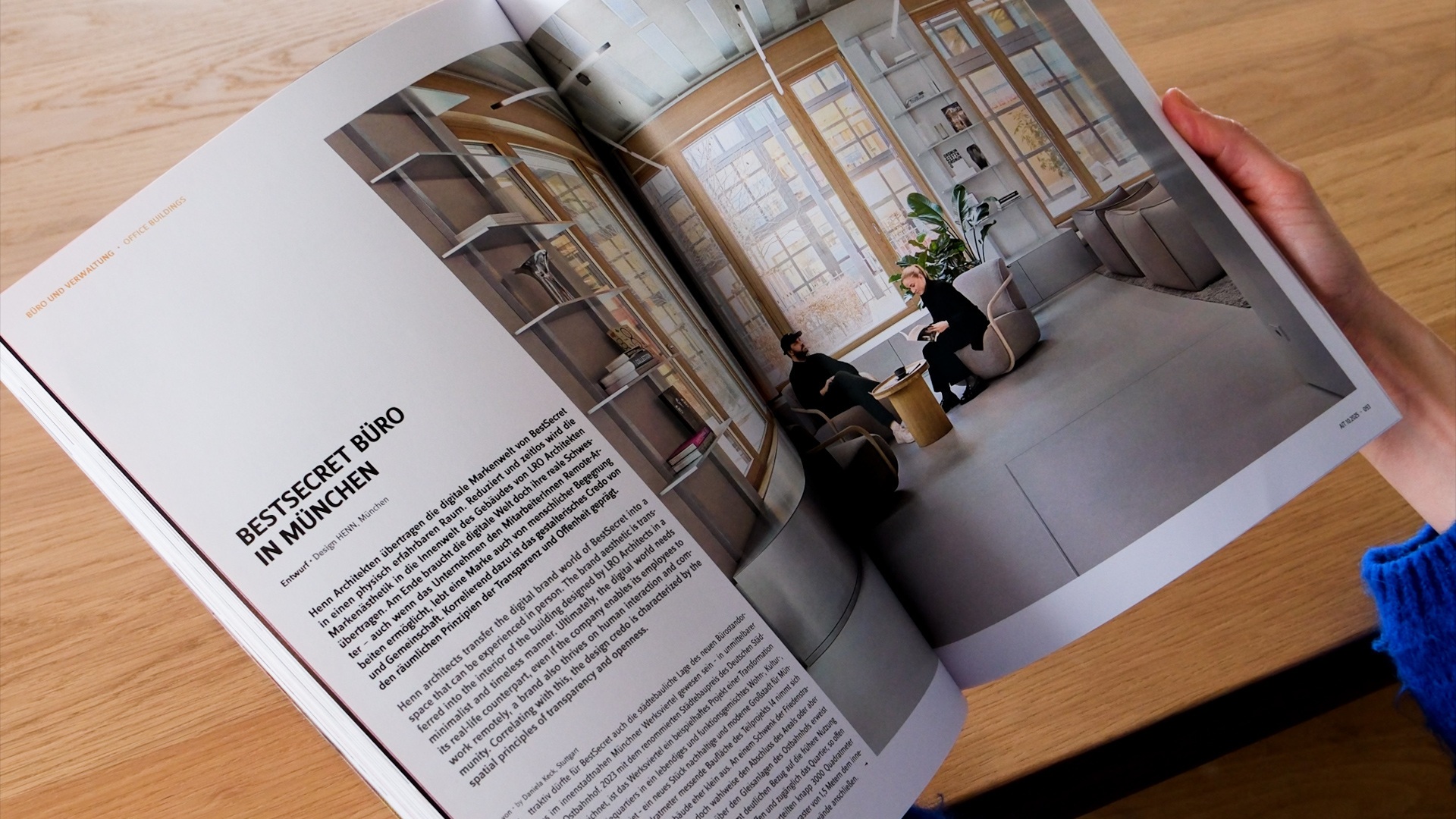 Eine Person liest eine Zeitschrift mit einem Artikel über ein Münchner Büro, in dem innovatives, nachhaltiges architektonisches Design und technische Integration hervorgehoben werden.