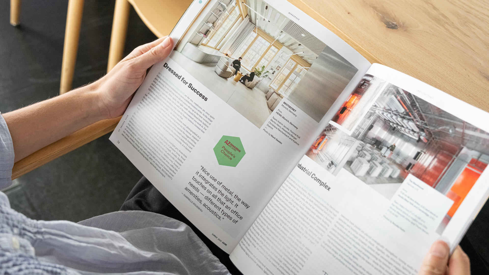 Individual reviewing a magazine featuring high-tech architectural projects, innovative research facilities, and sustainable industrial or educational building designs at a wooden table, highlighting advanced technology integration and forward-thinking environments.